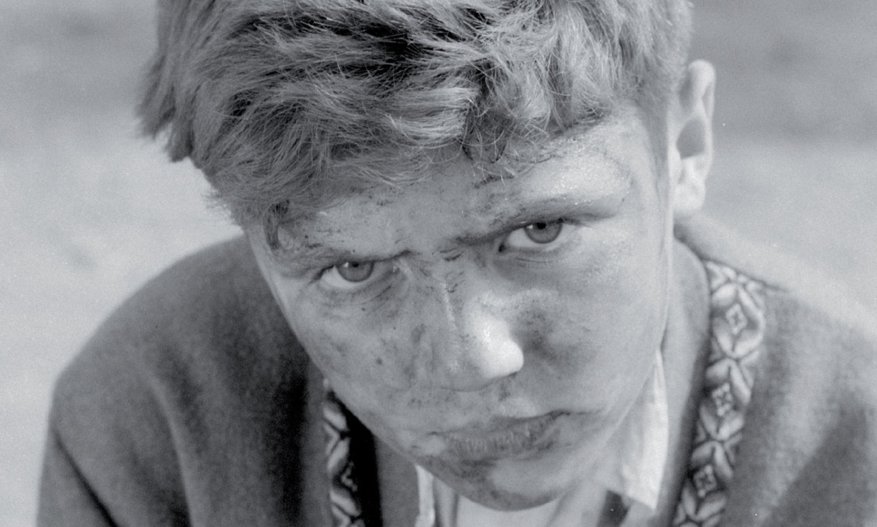 Image du film en noir et blanc. On y voit un garçon qui nous regarde dans les yeux.
