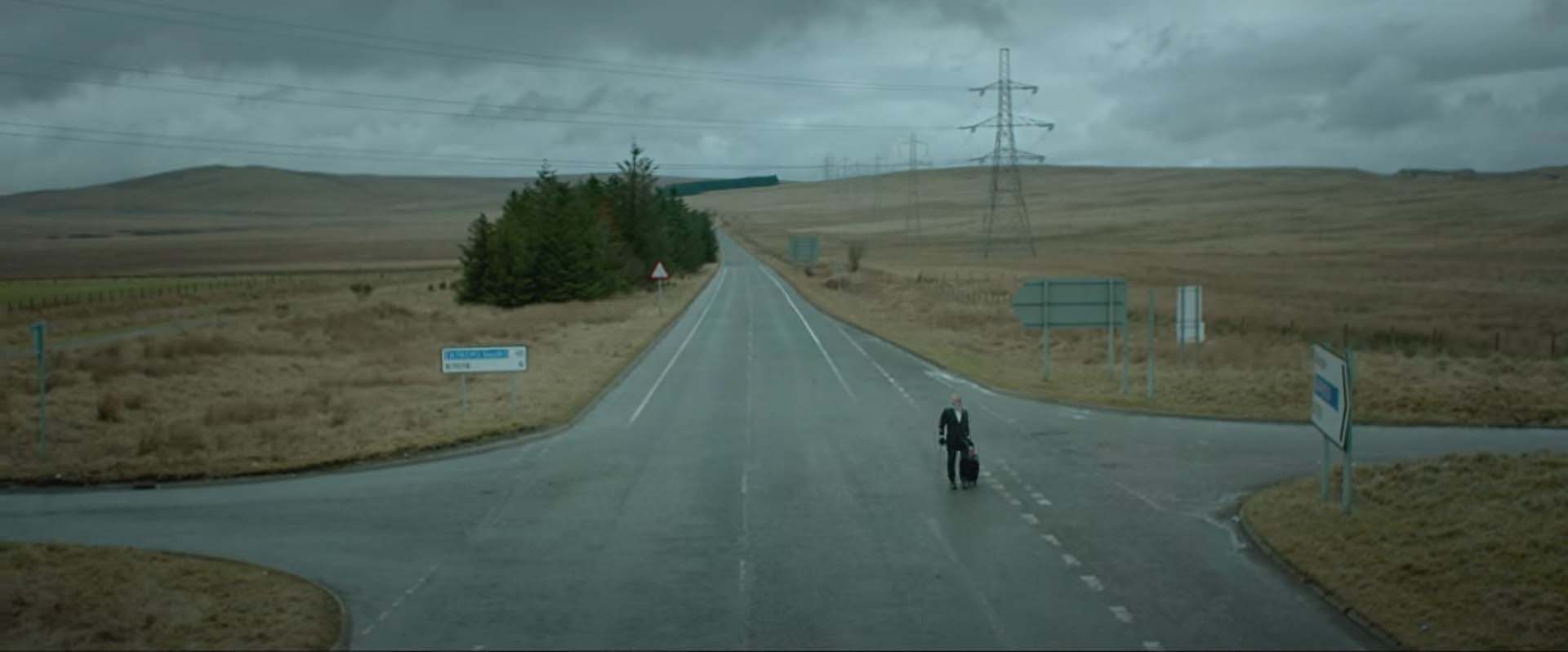 Peter Mullan dans Hector. Le héros est au croisement de routes désertes, dans la campagne anglaise.
