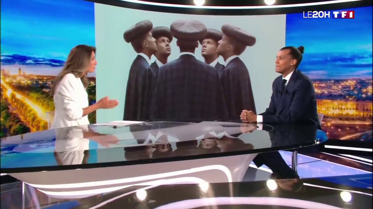 Image de Stromae sur le plateau de TF1 avec la pochette de son disque en arrière plan.