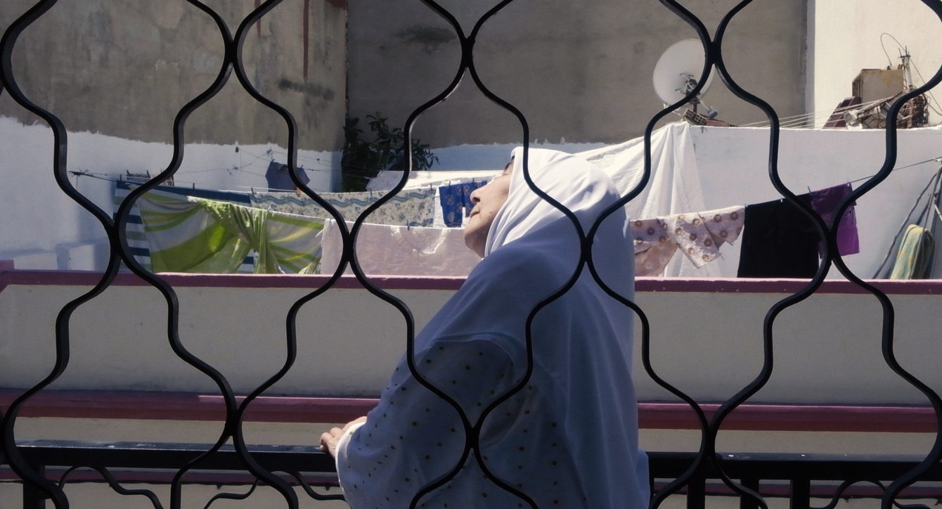 Une femme agée, portant un voile, regarde le ciel depuis son toit. Le linge sèche en arrière plan. Une image du film Les Miennes.